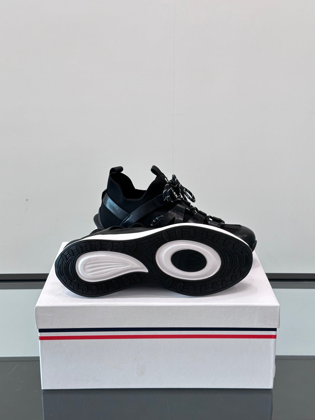 Black Moncler sneaker outsole view on box, with circular tread pattern and laces.