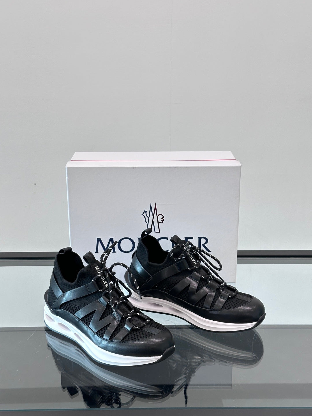Black Moncler sneakers, front view with lace-up closure and white outsole edge contrast.