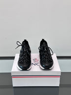 Pair of black Moncler lace-up sneakers on a box, showing side stripes and laces.