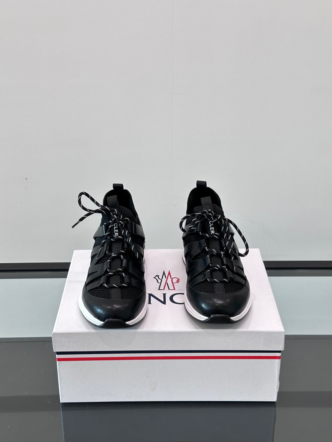 Pair of black Moncler lace-up sneakers on a box, showing side stripes and laces.