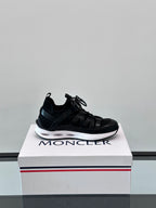 Black Moncler lace-up sneaker on box, side profile with stacked sole and logo mark.