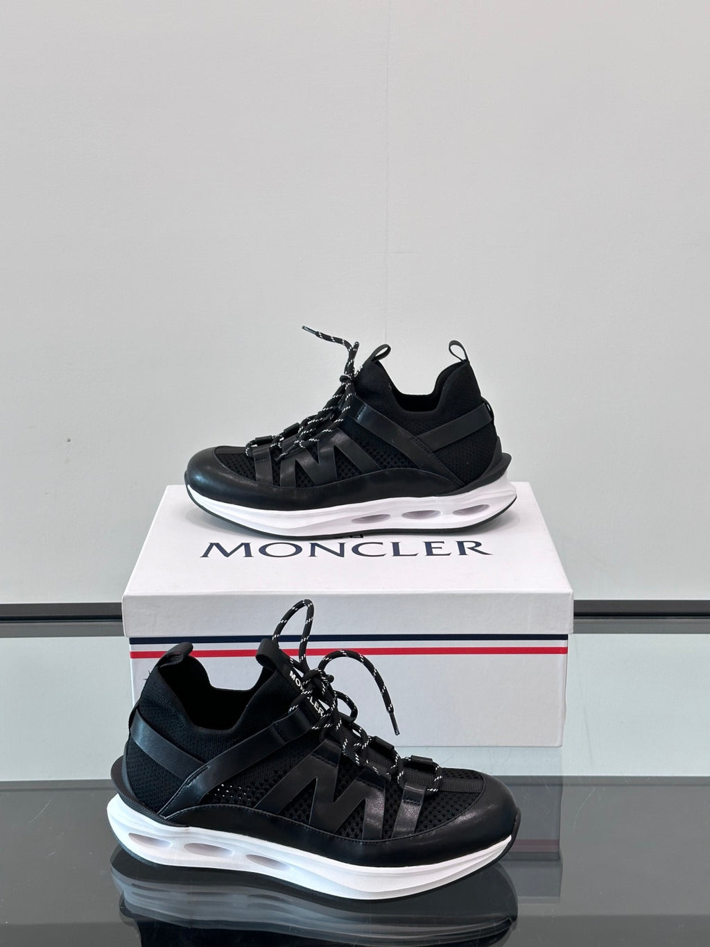 Moncler black lace-up sneaker with sculpted sole and side logo detail; box visible.