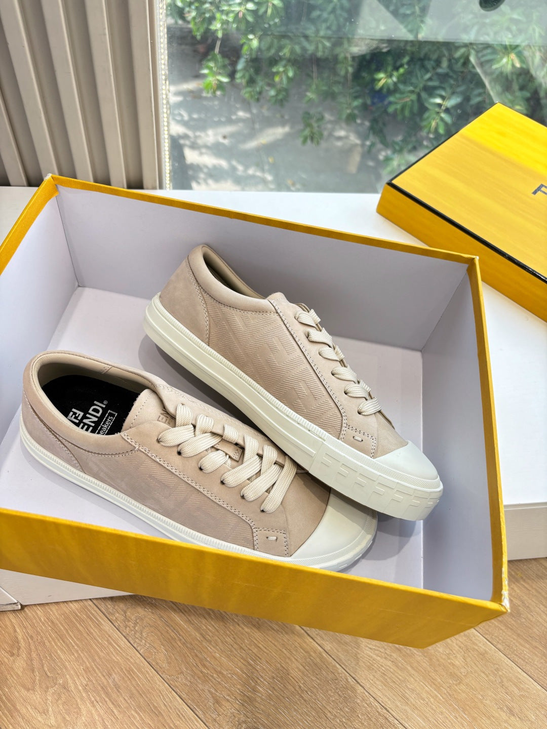 Beige lace-up sneakers with white sole, placed in an open shoe box.