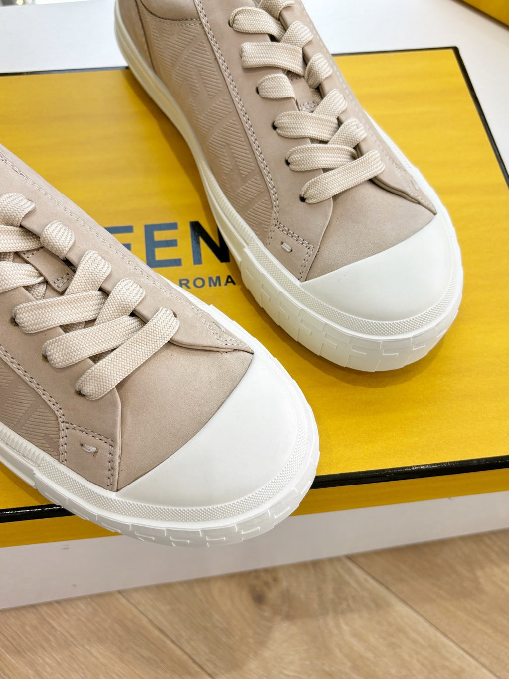 Beige sneakers close-up showing laces and textured side panels, white sole.