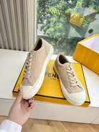 Beige lace-up sneaker held in hand beside matching pair; FENDI branding on box.