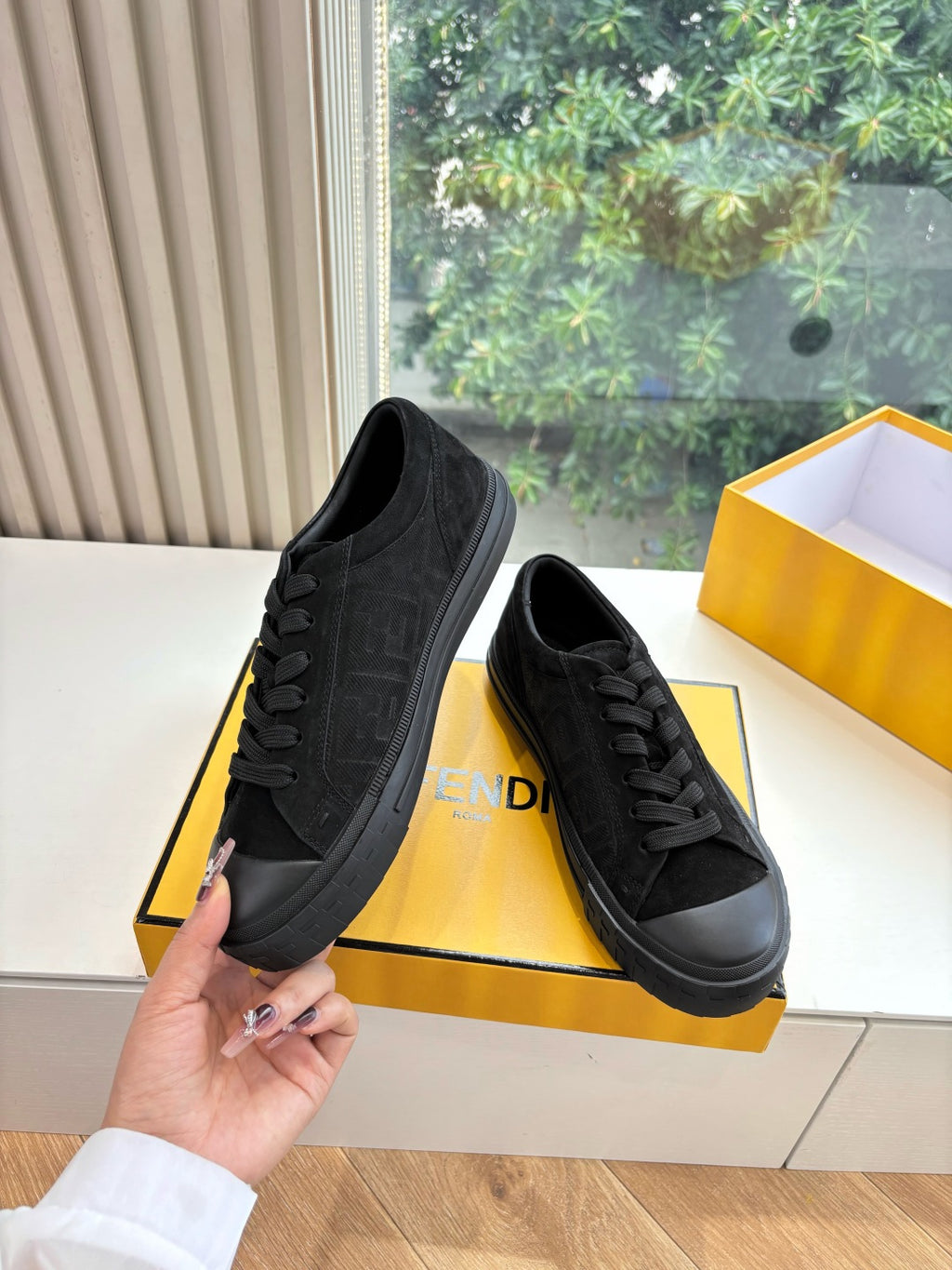 Black Fendi low-top sneakers with lace-up closure, held above the box