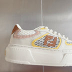 White unisex sneakers with brown, yellow, and pink emblem patch and thick sole
