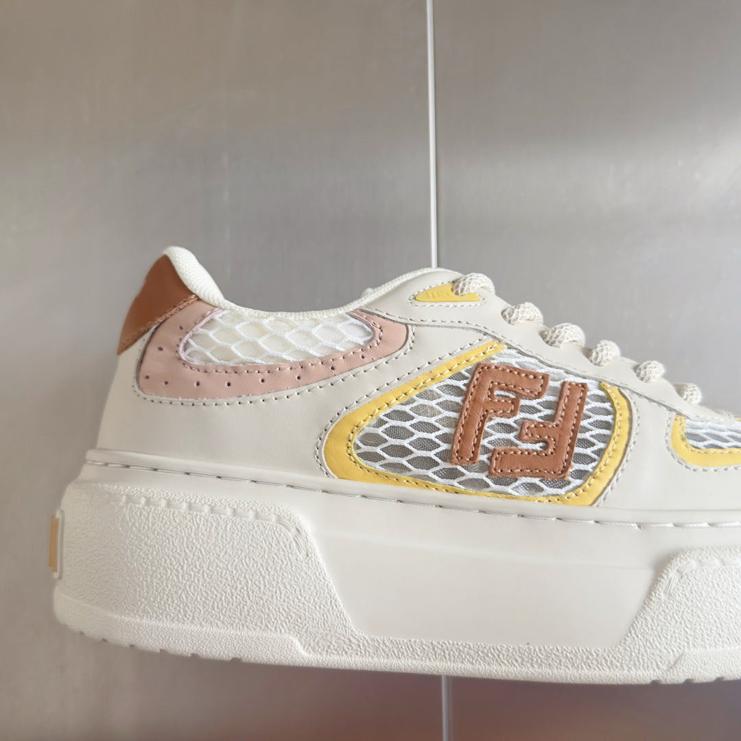 White unisex sneakers with brown, yellow, and pink emblem patch and thick sole
