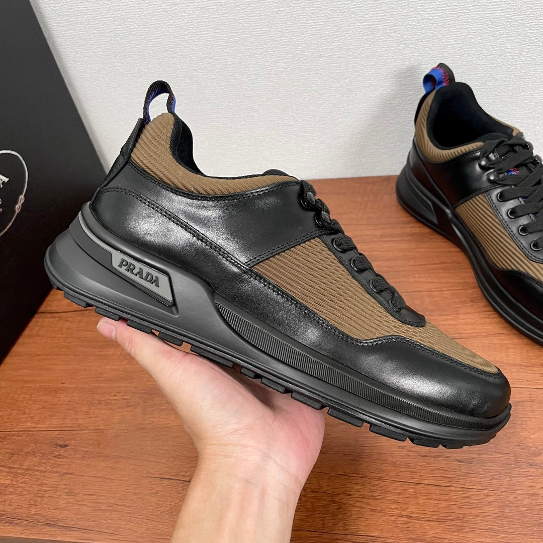 Prada unisex sneakers held by hand, black leather with tan side panel and logo