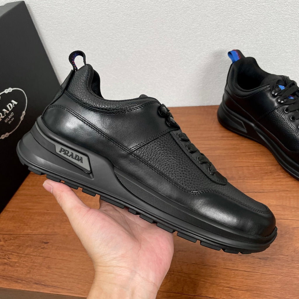 Prada unisex side view sneaker held in hand, black leather with PRADA logo plate