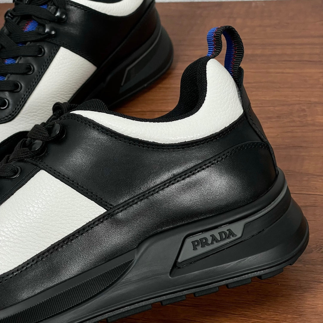 Prada unisex sneaker side close-up, black leather trim, white panel, PRADA badge on midsole