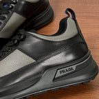 Prada unisex sneaker close-up, black leather with PRADA logo badge on midsole