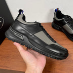 Prada unisex sneaker held side-up, black leather with gray panels and PRADA logo