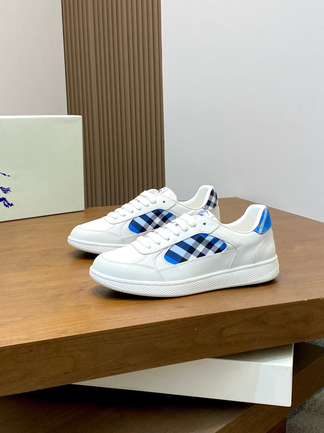 Pair of white sneakers on a shelf with blue check inserts and blue heel tabs