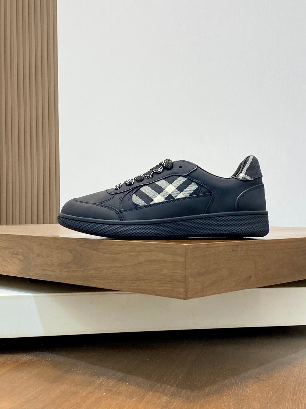 Burberry low-top sneakers on display, dark upper with check stripe and blue sole