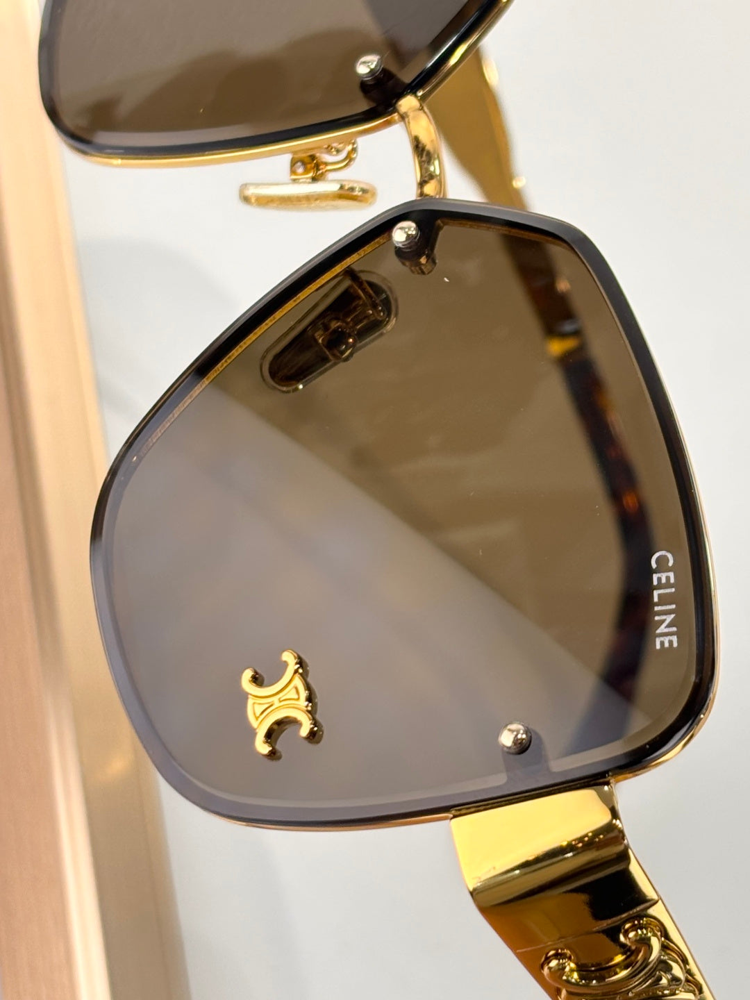 Celine sunglasses close-up of dark tinted lens with gold frame and decorative emblem