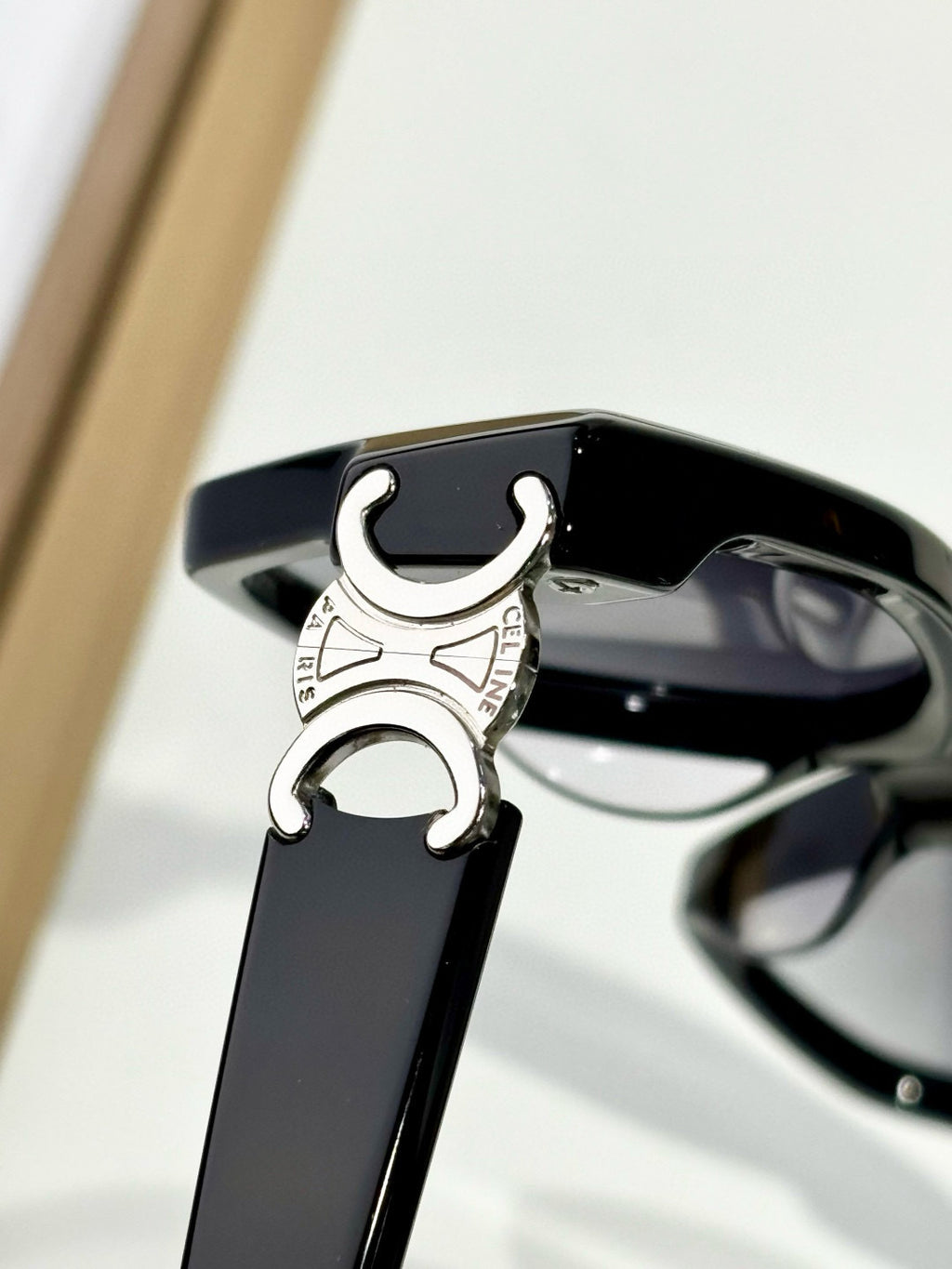 Close-up of black eyeglasses temple with silver C emblem and hinge detail