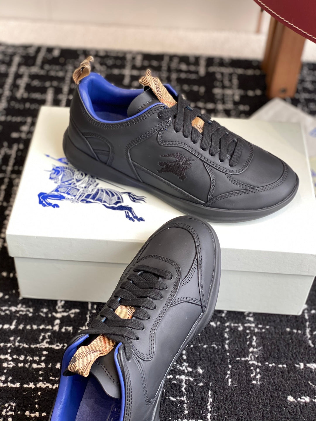 Black low-top sneakers with blue interior and tan lace-tab accents, worn-solo view