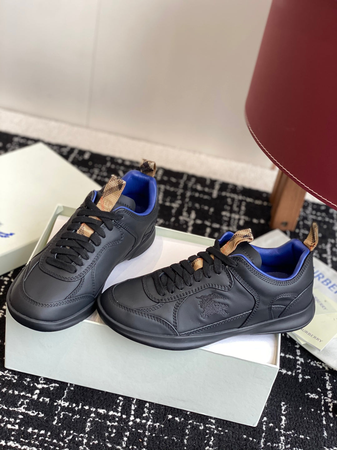 Black low-top sneakers with blue interior and tan lace-tab accents, angled view