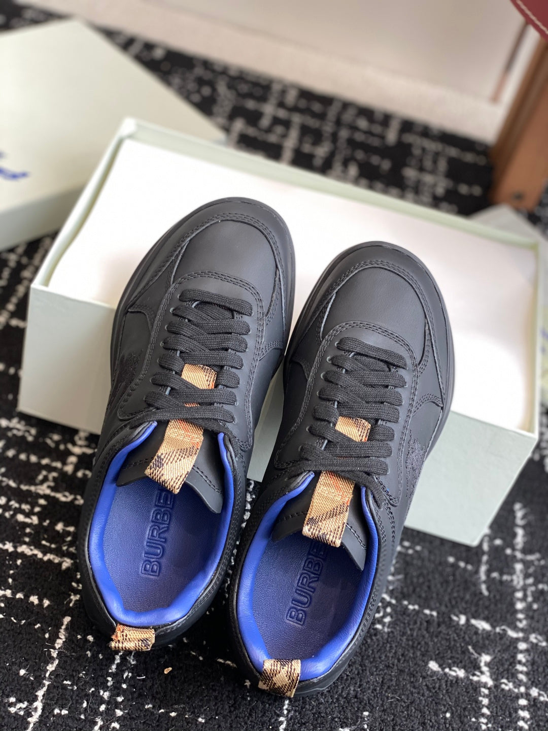 Black low-top sneakers with blue lining and tan lace-tab detail, front view