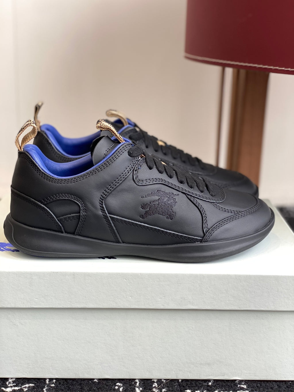 Black low-top sneakers with blue lining and tan lace-tab detail, side view