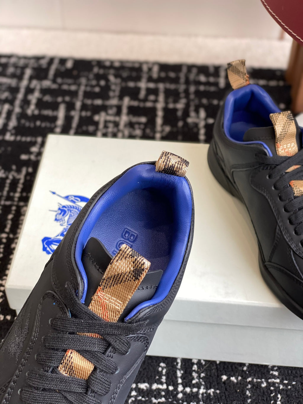 Black low-top sneaker with blue interior and tan lace-tab accents, toe and tongue close-up