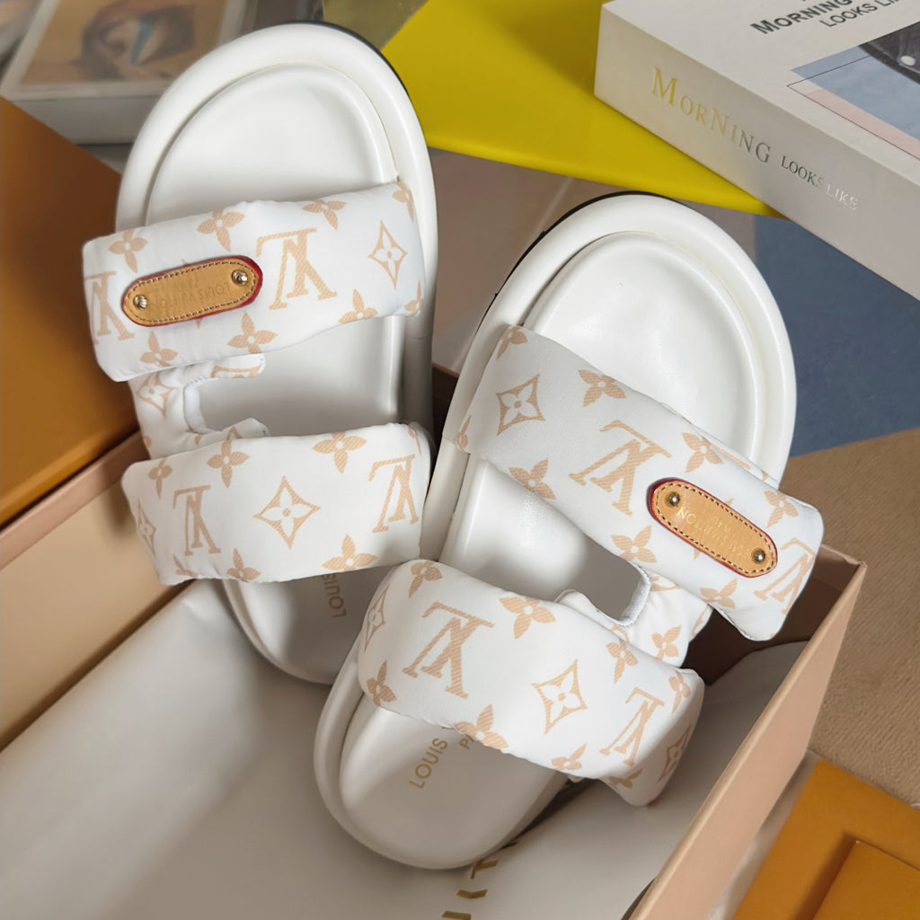 Close-up of white monogram slide sandals with tan logo patch on upper straps