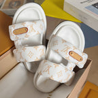 Close-up of white monogram slide sandals with tan logo patch on upper straps