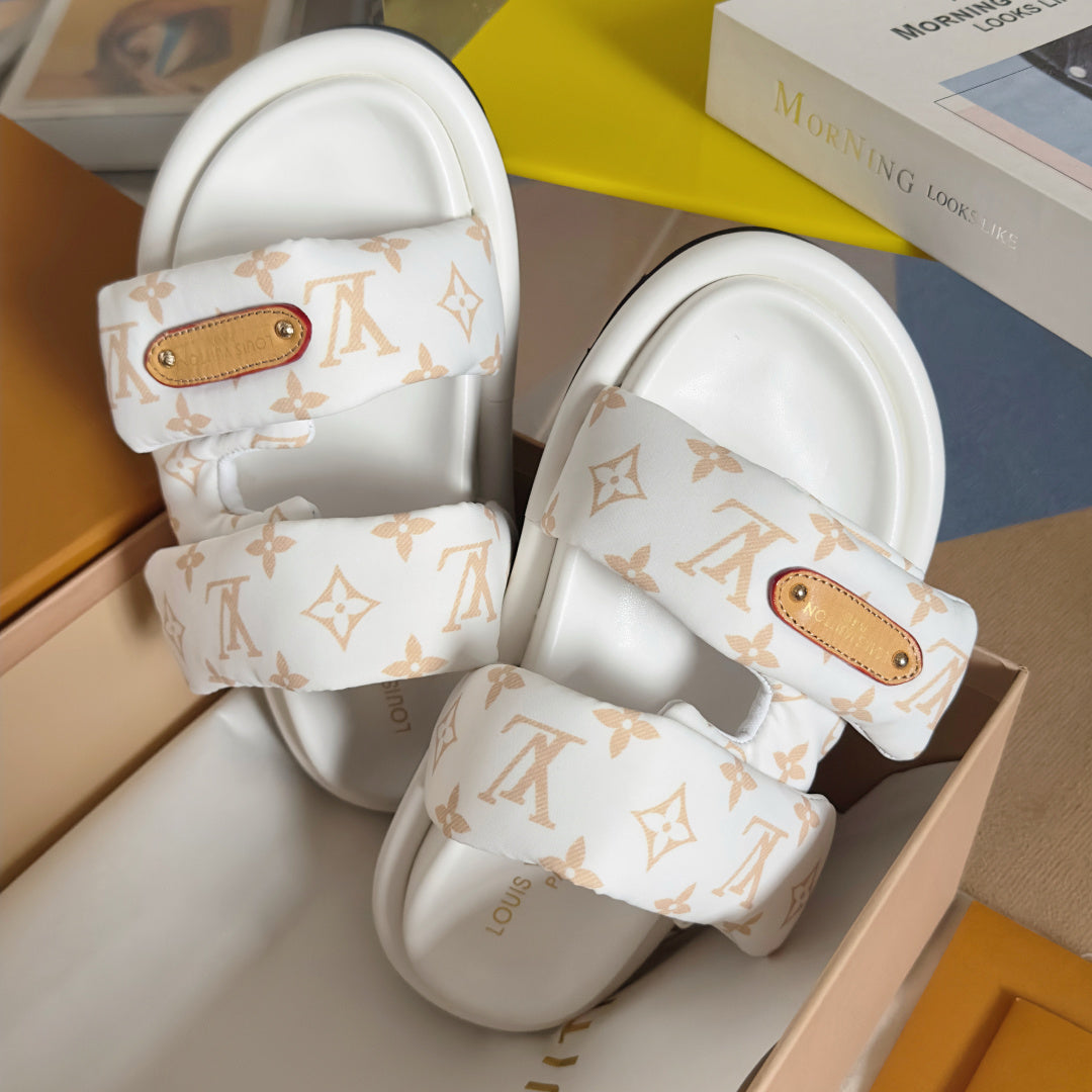 Close-up of white monogram slide sandals with tan logo patch on upper straps