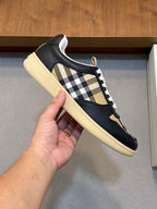 Single sneaker held by hand, navy upper with check side and white lace trim