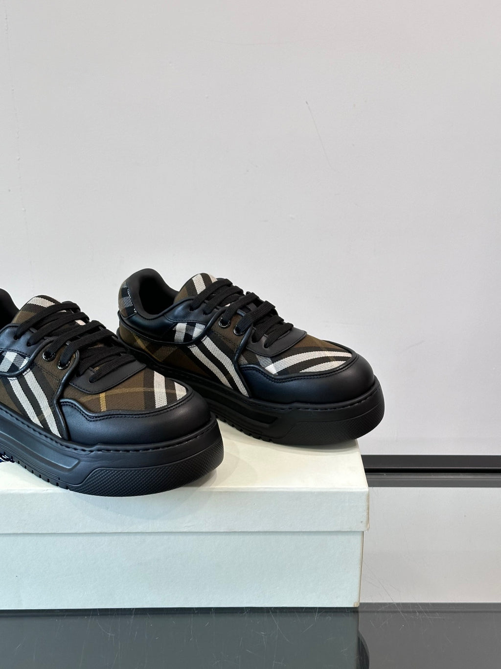 Two dark navy lace-up sneakers on a box, beige plaid and white stripe accents