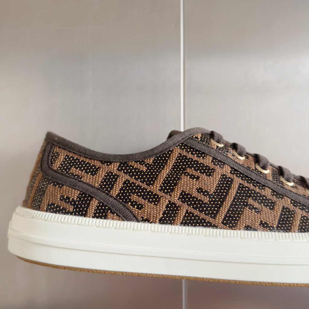 Close-up of Fendi lace-up sneaker upper, brown FF logo pattern, white midsole edge.