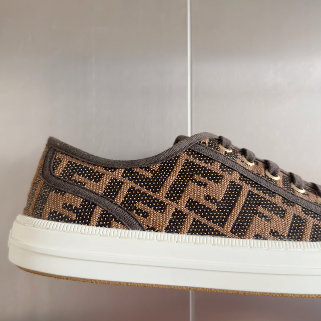 Close-up of Fendi lace-up sneaker upper, brown FF logo pattern, white midsole edge.