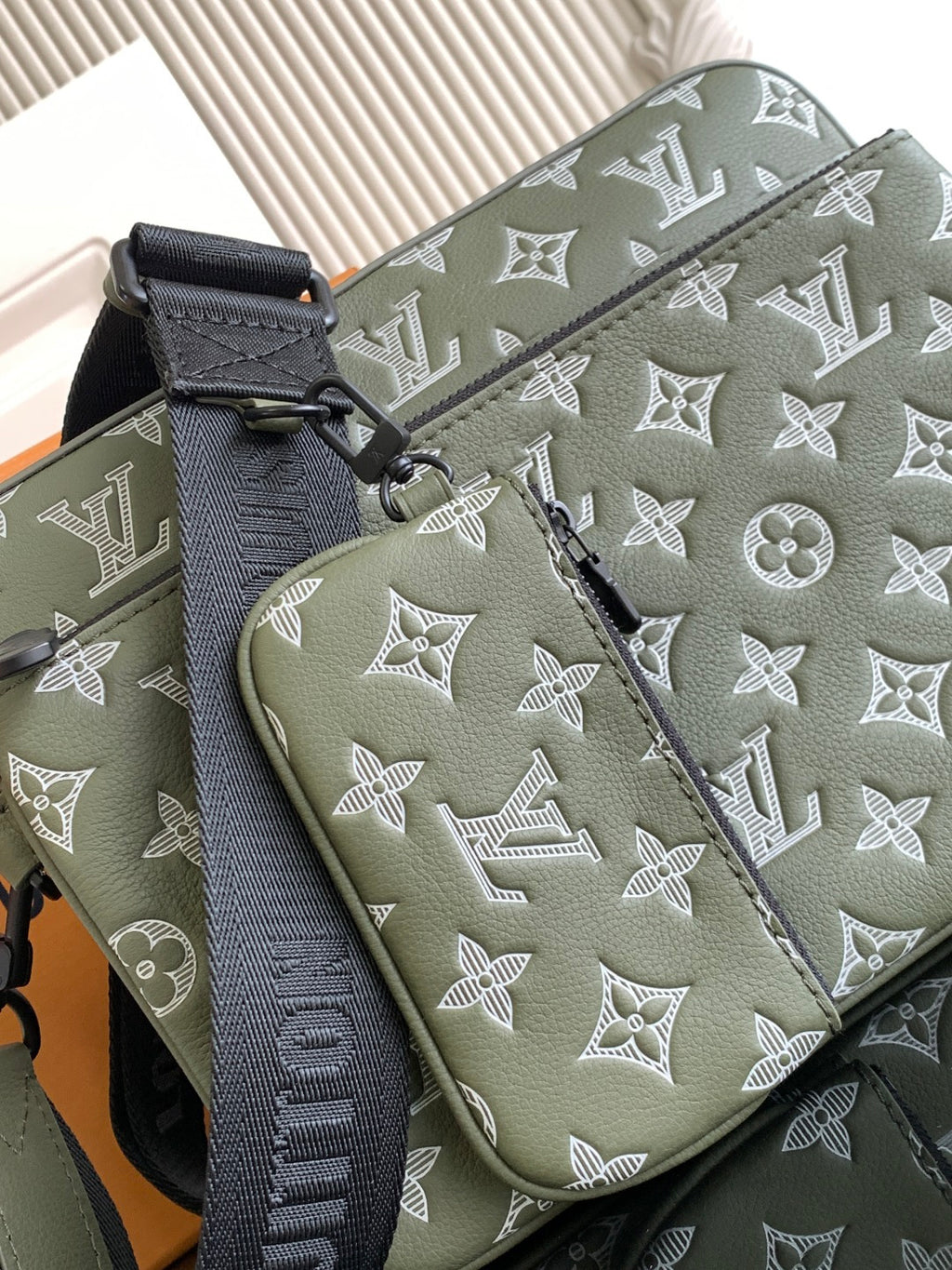 Olive green bag panel with white monogram print, textured strap and visible edge stitching