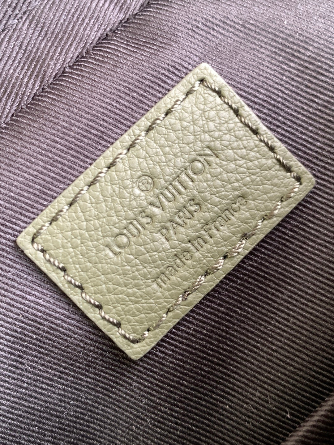 Light green leather label on bag with embossed Louis Vuitton Paris text
