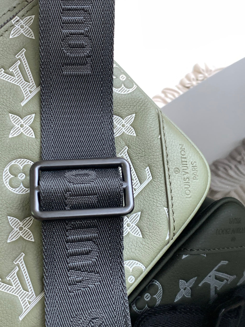 Olive green bag with dark patterned shoulder strap and rectangular metal buckle