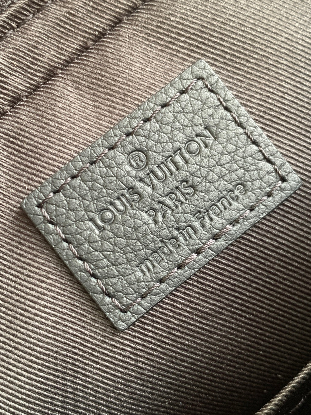 Leather interior label with embossed Louis Vuitton Paris text, stitched dark.