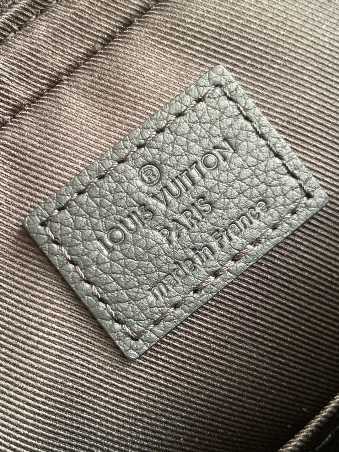 Leather interior label with embossed Louis Vuitton Paris text, stitched dark.