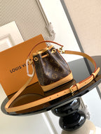 Louis Vuitton monogram bucket bag with tan crossbody strap and gold-tone clasp