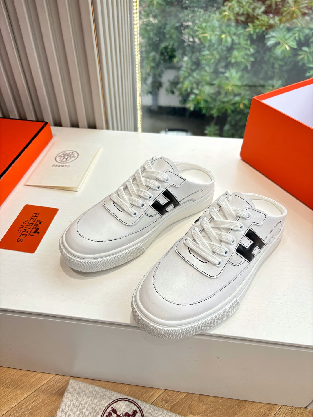 White leather sneakers with black H buckle-style logo, stitched toe and laces