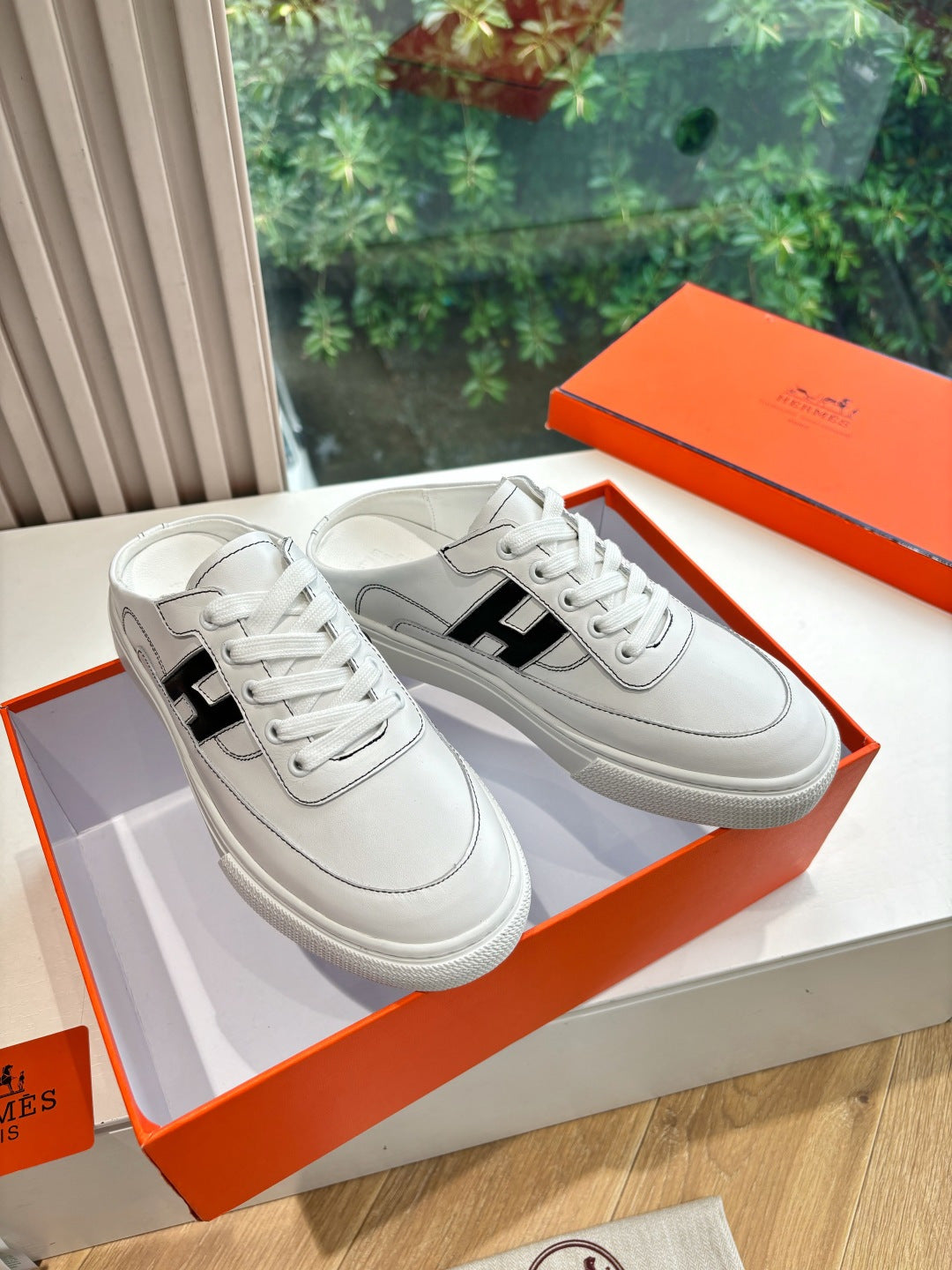 White leather sneakers with black H logo and white laces, low-profile sole