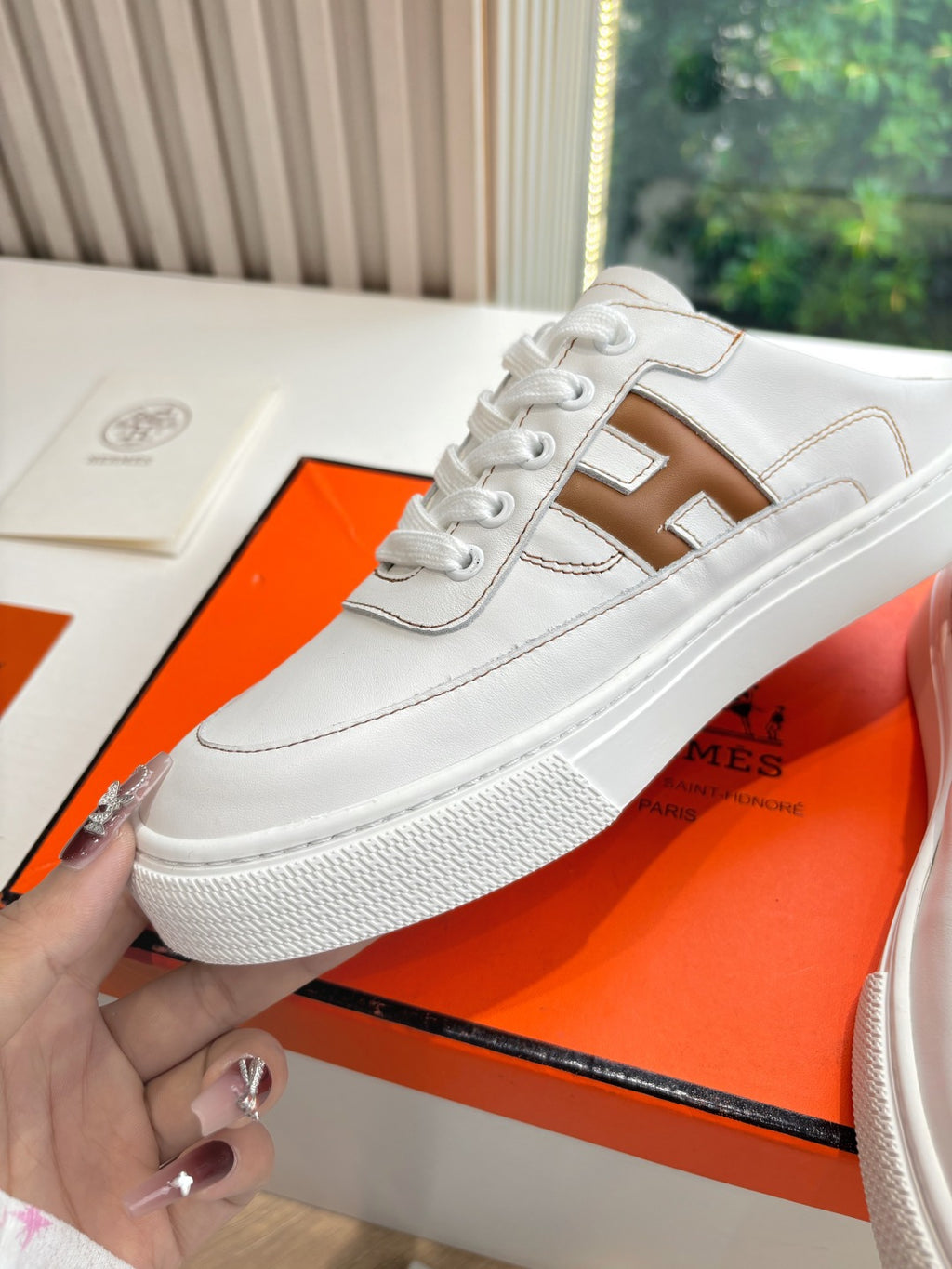 White Hermes sneaker with brown H logo on side, laced upper close-up