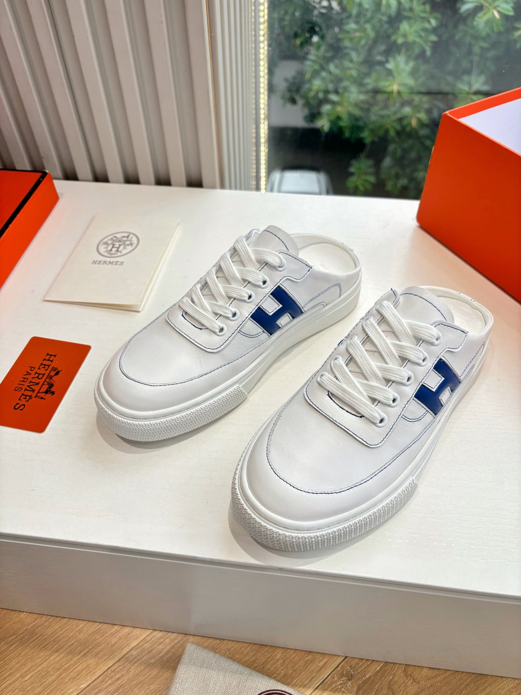 White leather sneakers with blue H emblem, lace-up front view