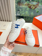 White sneakers held up by hand, blue H side logo, lace-up style