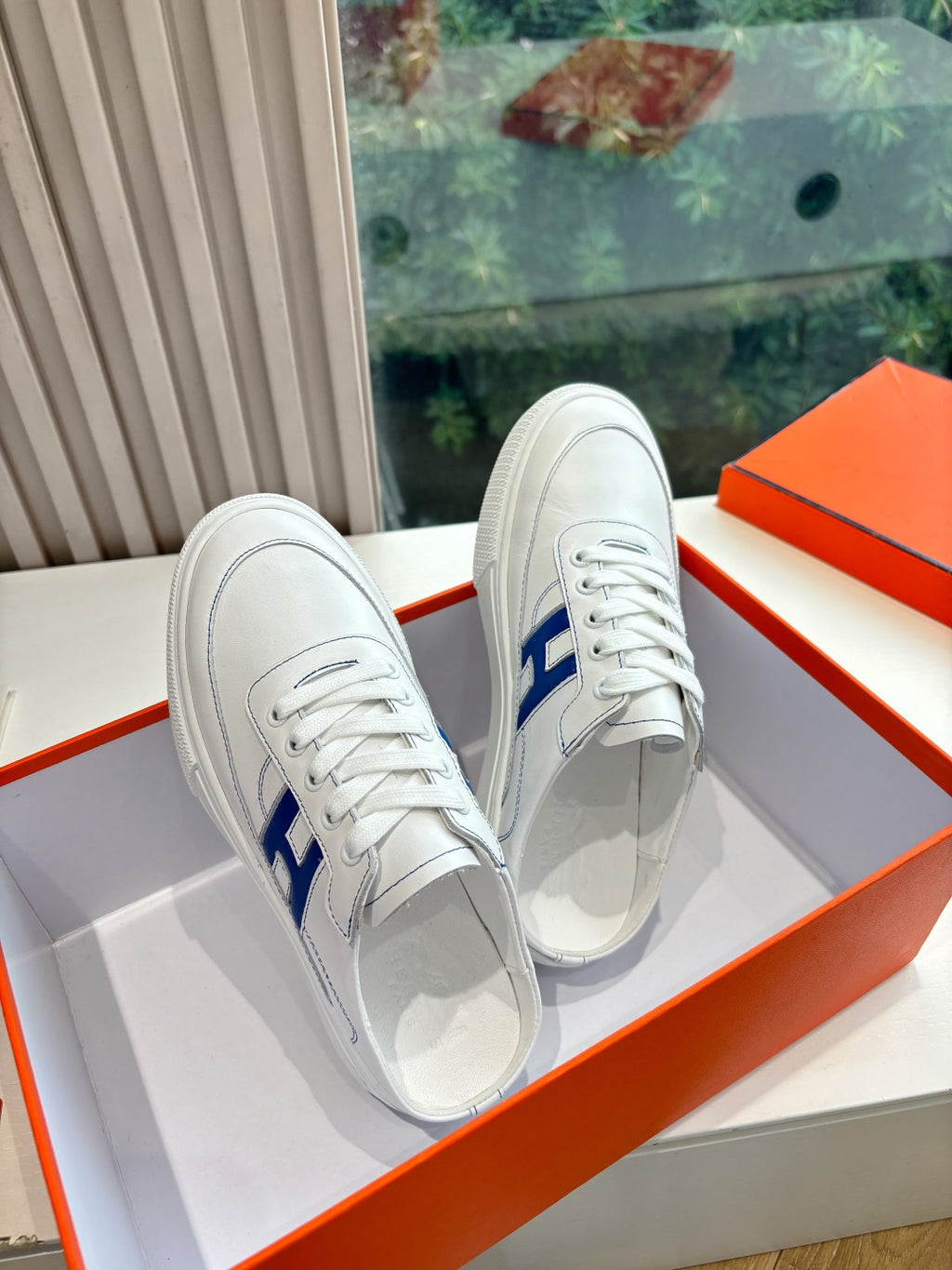 Pair of white low-top sneakers with blue H side logo and lace-up design
