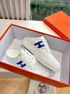 White low-top sneakers in a box, blue H logo on the side panels