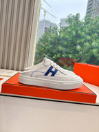 White low-top sneakers with blue H logo resting on a display box