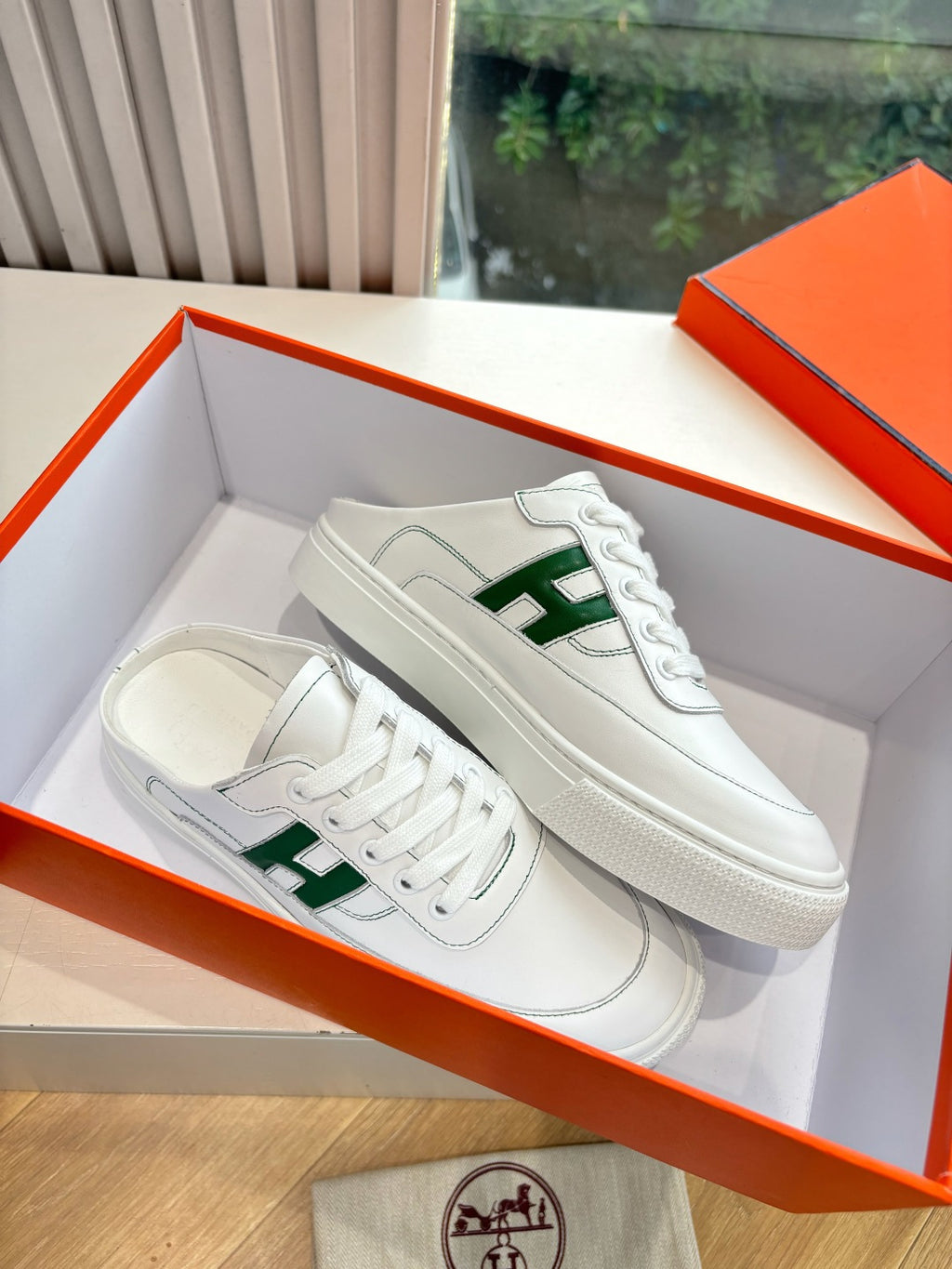 White sneakers with green H logos, side-by-side in open orange shoebox