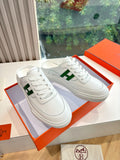 White low-top sneakers with green H logo on side, in orange shoebox