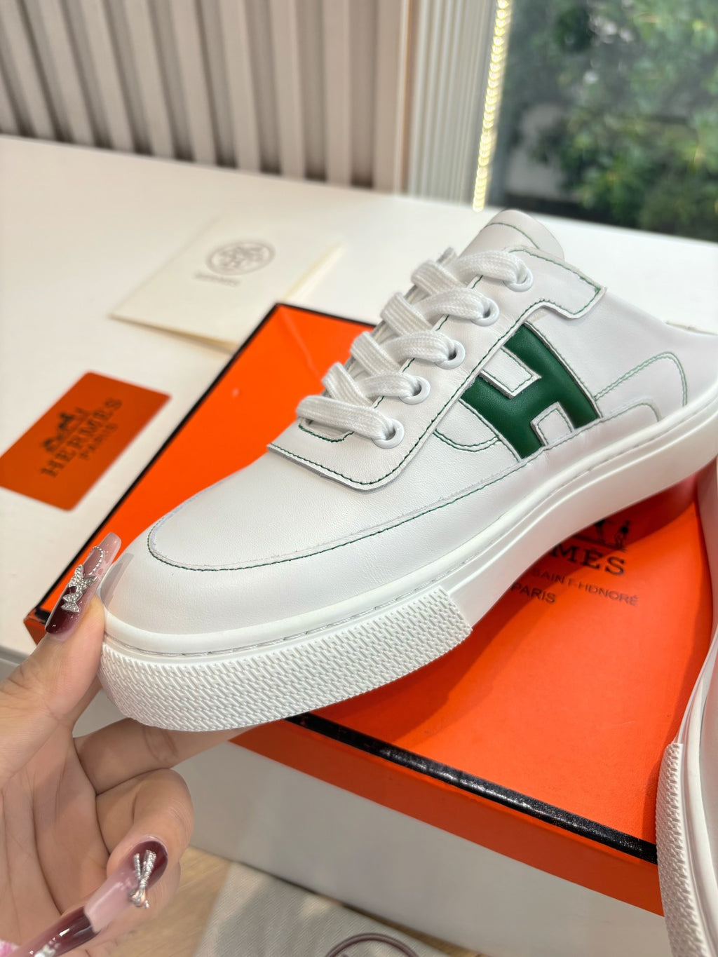 White low-top sneaker with green H logo strap and lace-up, close-up